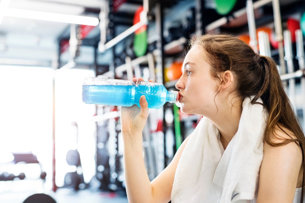 Young fitness girl with dental braces drinking water from a bottle at the gym after a hard workout